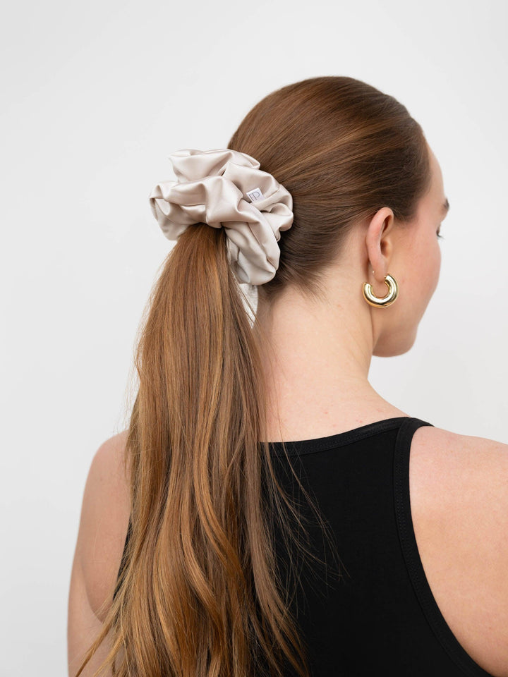 Woman styling her hair with a champagne satin scrunchie in a sleek ponytail