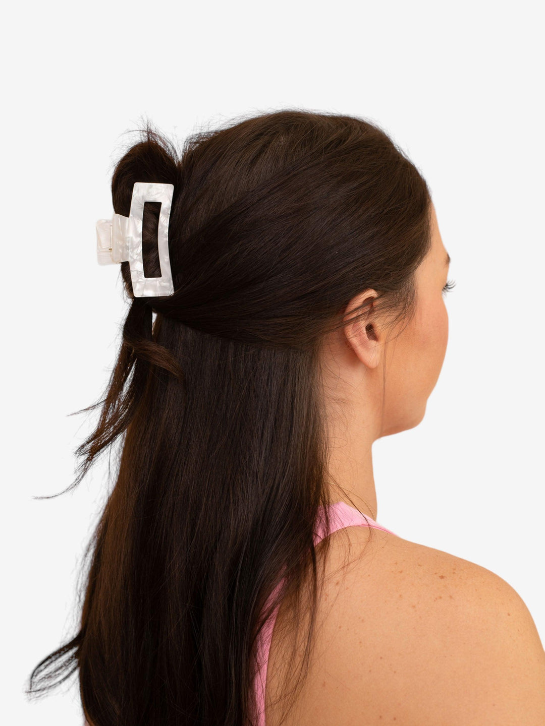 Brunette model with thick hair using small (basic) claw clip in white pearl to hold a half-up hairstyle.