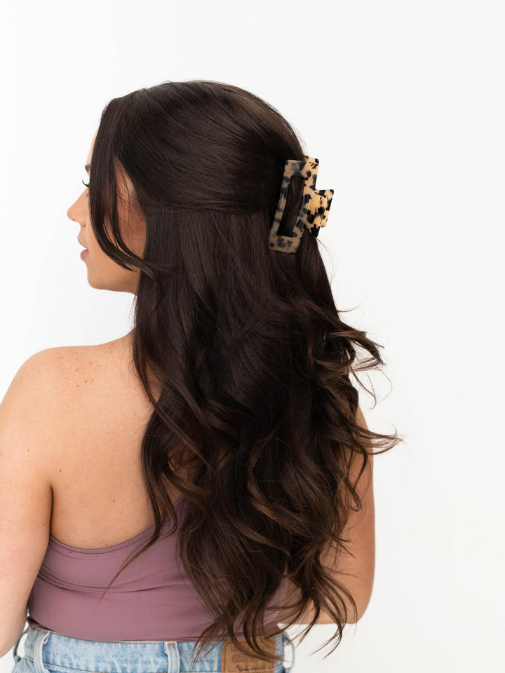 Brunette model with thick hair using Next Level claw clip in light tortoise shell to hold a half-up hairstyle.